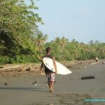 Surfeur sur la plage de sable noir du village de Cahuita au Costa Rica